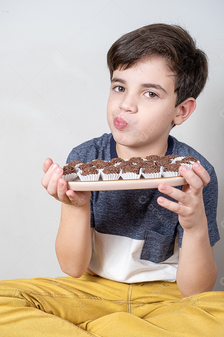 Criança de 9 anos segurando uma bandeja com várias bolas de chocolate e franzindo os lábios.