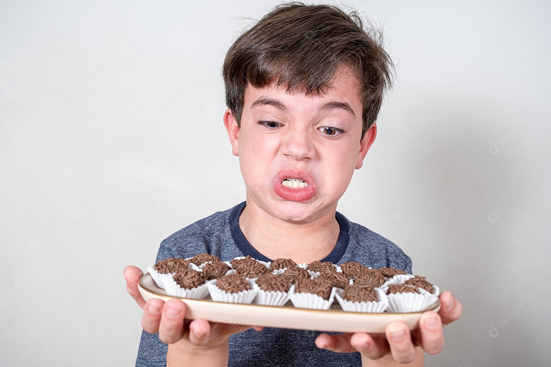 Brasileiro de 9 anos segurando uma bandeja com vários bombons brasileiros e fazendo cara de brava.