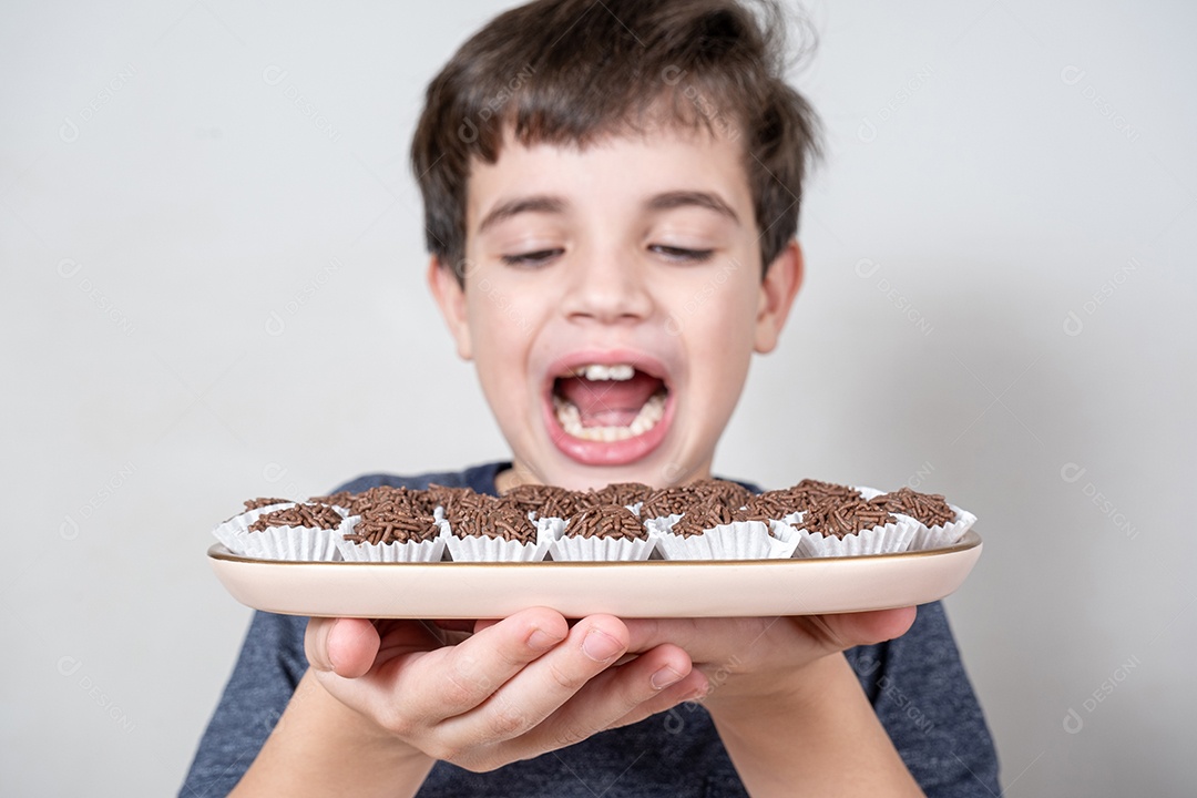 Várias bolas de chocolate brasileiras em uma bandeja. No fundo desfocado, criança com a boca aberta.
