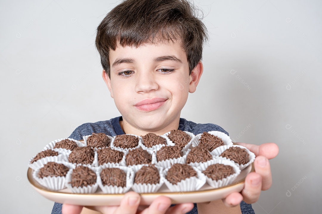 Brasileiro de 9 anos olhando para uma bandeja com várias bolas de chocolate brasileiras e fazendo uma cara de desapontado.
