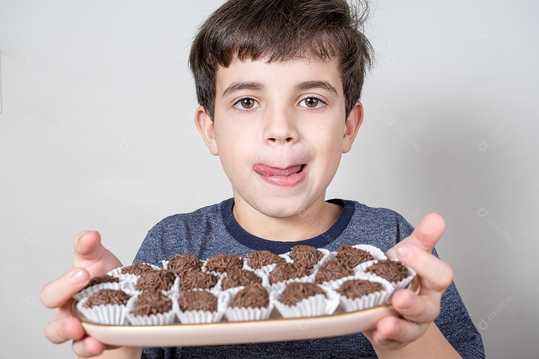 Brasileiro de 9 anos segurando uma bandeja com várias bolas de chocolate e lambendo os lábios.