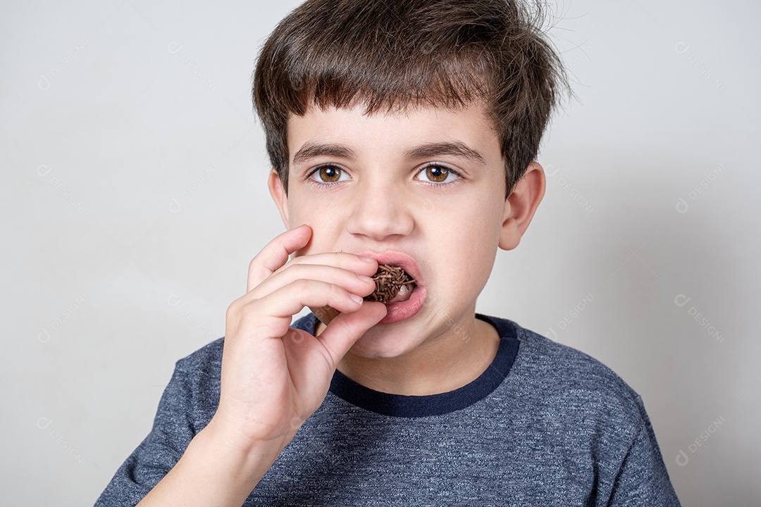 Brasileiro de 9 anos comendo uma bola de chocolate brasileira e de frente para a câmera.
