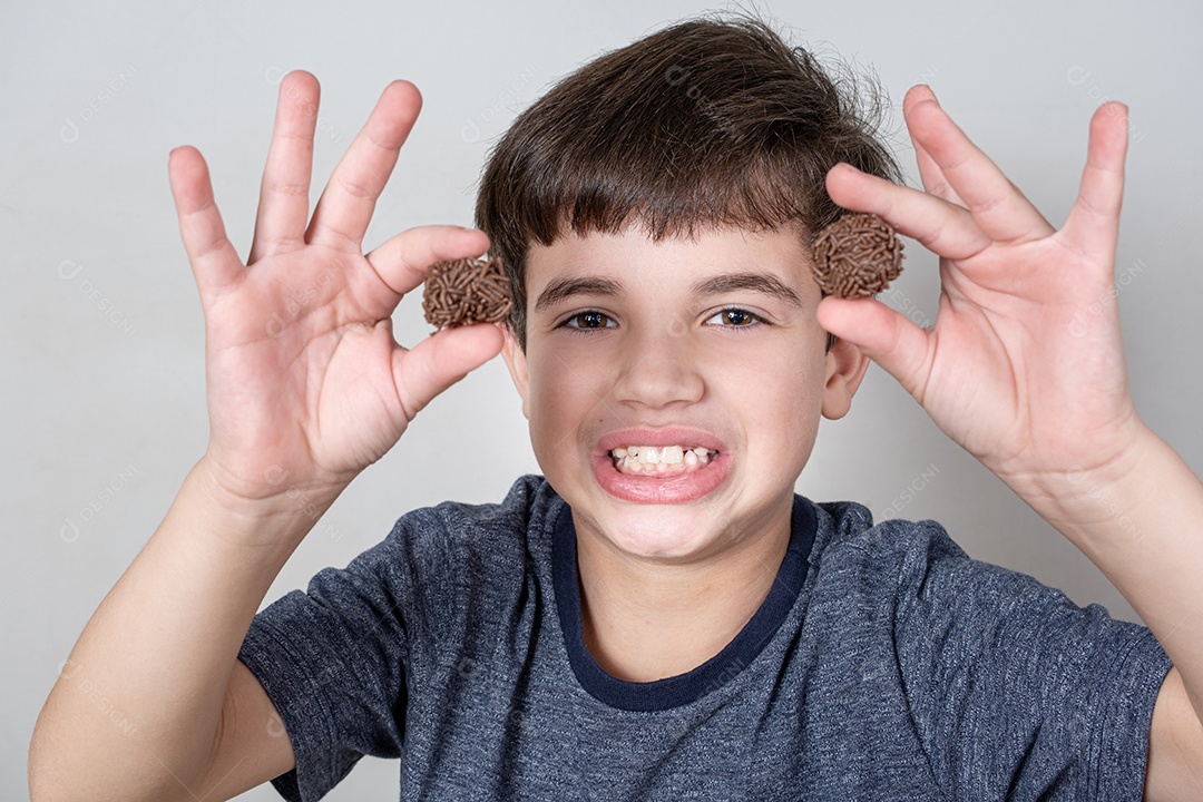 Brasileiro de 9 anos mostrando os dentes e segurando duas bolas de chocolate brasileiras.