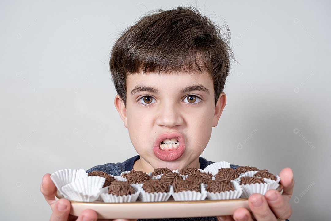 Criança de 9 anos segurando uma bandeja com várias bolas de chocolate brasileiras e rangendo os dentes.