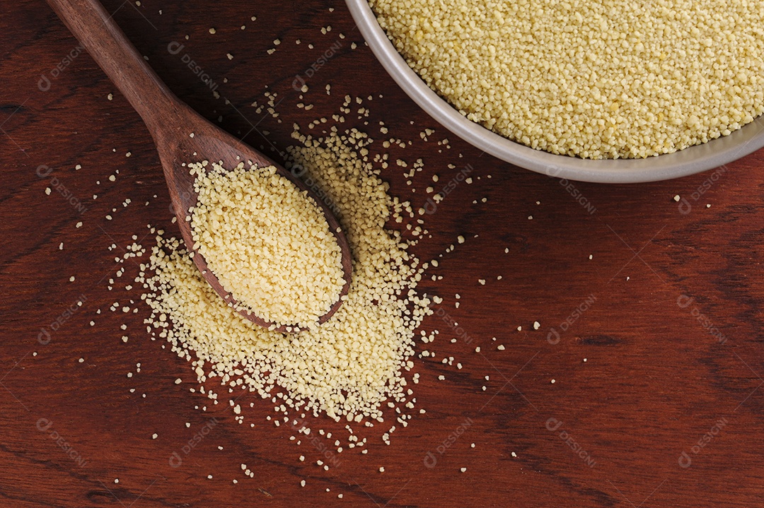 Grãos de cuscuz em colher de pau em fundo de madeira. Espaço para texto.
