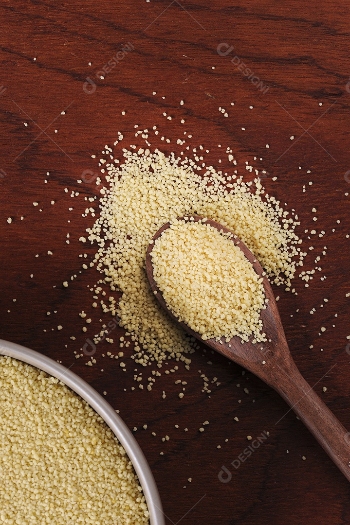 Grãos de cuscuz em colher de pau em fundo de madeira. Espaço para texto.