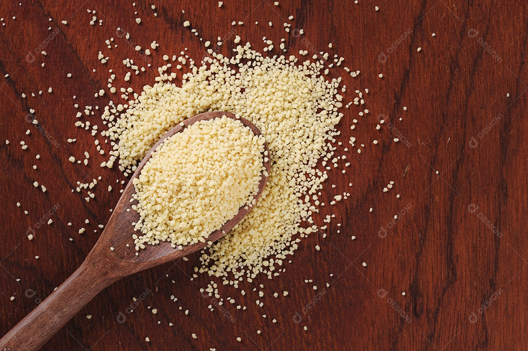 Grãos de cuscuz em colher de pau em fundo de madeira. Espaço para texto.
