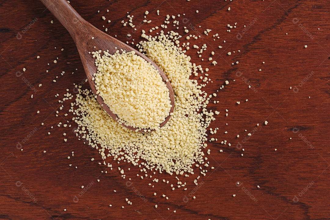 Grãos de cuscuz em colher de pau em fundo de madeira. Espaço para texto.