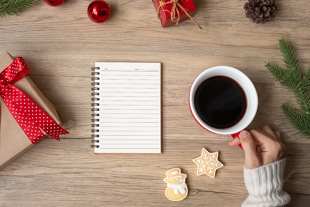 Mão de uma mulher segurando uma xícara de café preta com um caderno em branco