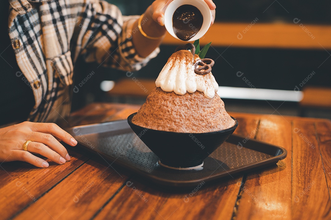 Mulher coreana sentada em lanchonete colocando calda de chocolate na sobremesa gelada - bingsu do chocolate