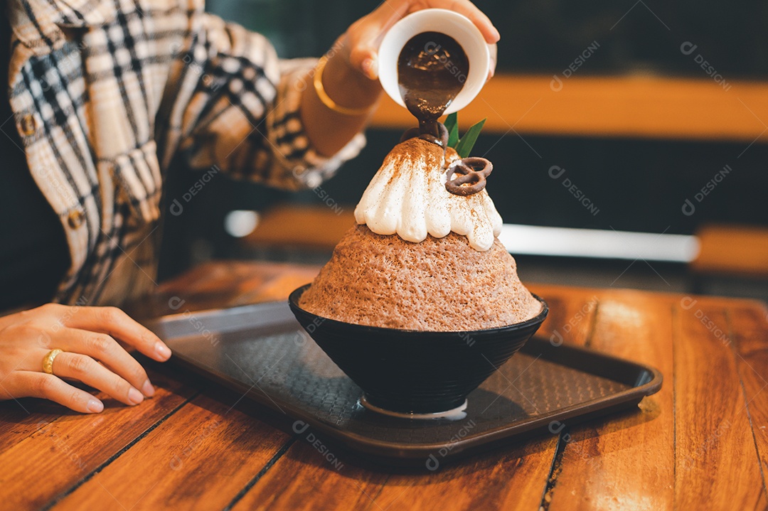 Mulher coreana sentada em lanchonete colocando calda de chocolate na sobremesa gelada - bingsu do chocolate