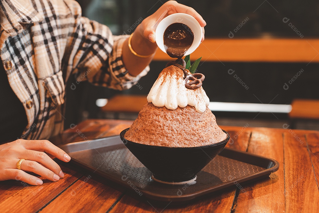 Mulher coreana sentada em lanchonete colocando calda de chocolate na sobremesa gelada - bingsu do chocolate