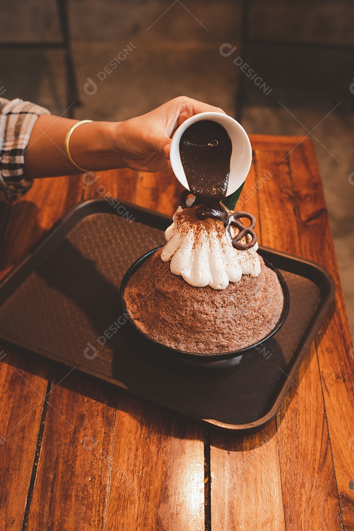 Mulher coreana sentada em lanchonete colocando calda de chocolate na sobremesa gelada - bingsu do chocolate