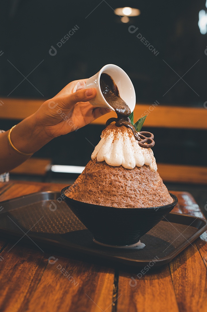 Mulher coreana sentada em lanchonete colocando calda de chocolate na sobremesa gelada - bingsu do chocolate