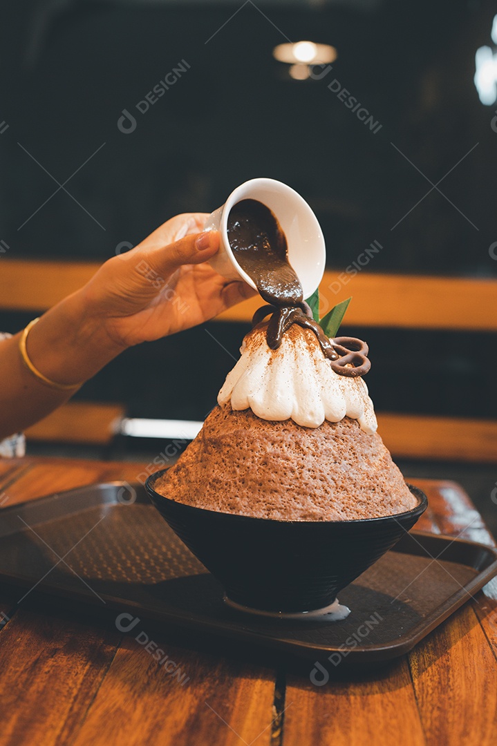 Mulher coreana sentada em lanchonete colocando calda de chocolate na sobremesa gelada - bingsu do chocolate