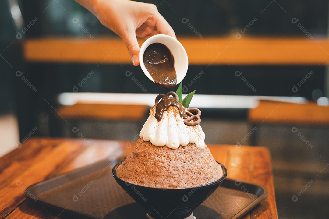 Mulher coreana sentada em lanchonete colocando calda de chocolate na sobremesa gelada - bingsu do chocolate