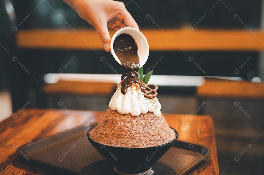 Mulher coreana sentada em lanchonete colocando calda de chocolate na sobremesa gelada - bingsu do chocolate