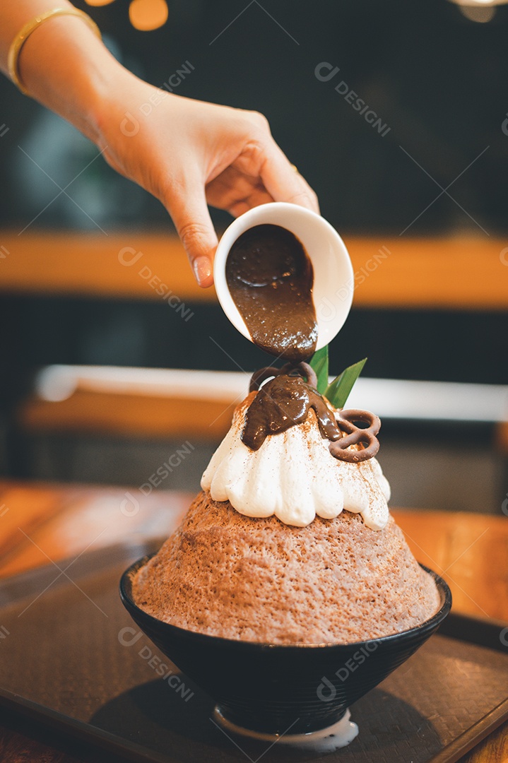 Mulher coreana sentada em lanchonete colocando calda de chocolate na sobremesa gelada - bingsu do chocolate
