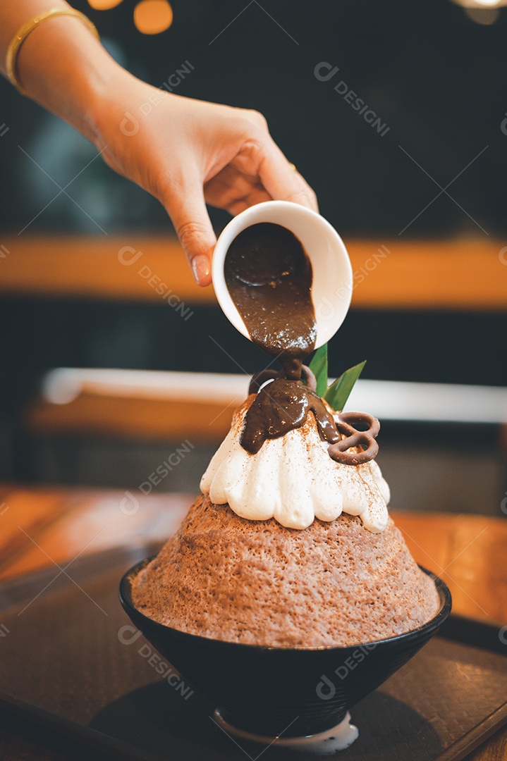 Mulher coreana sentada em lanchonete colocando calda de chocolate na sobremesa gelada - bingsu do chocolate