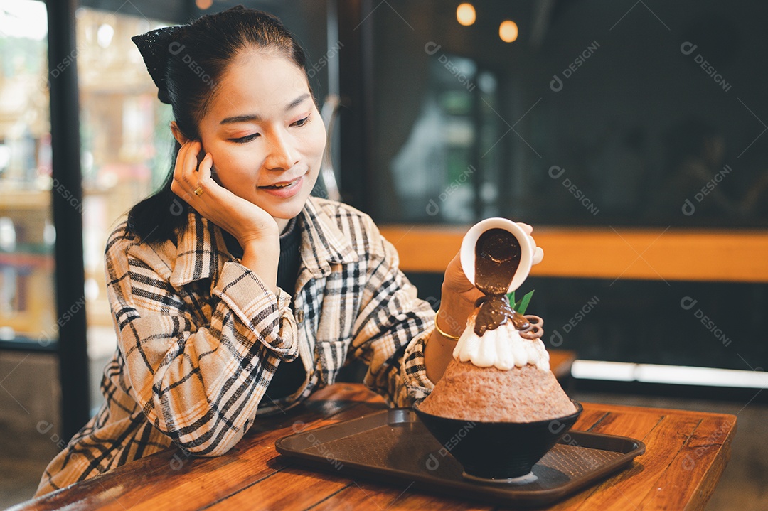 Mulher coreana sentada em lanchonete colocando calda de chocolate na sobremesa gelada - bingsu do chocolate