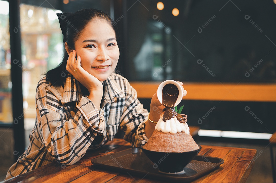 Mulher coreana sentada em lanchonete colocando calda de chocolate na sobremesa gelada - bingsu do chocolate