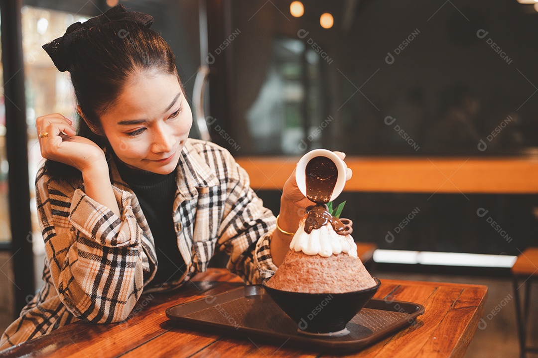 Mulher coreana sentada em lanchonete colocando calda de chocolate na sobremesa gelada - bingsu do chocolate