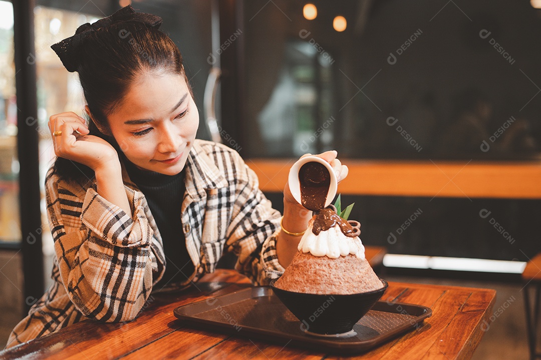 Mulher coreana sentada em lanchonete colocando calda de chocolate na sobremesa gelada - bingsu do chocolate