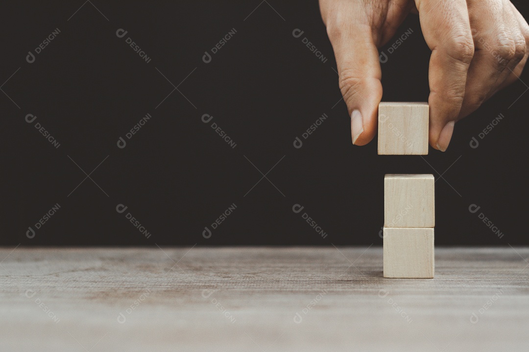 Mão organizando o empilhamento de blocos de madeira como escada na mesa de madeira