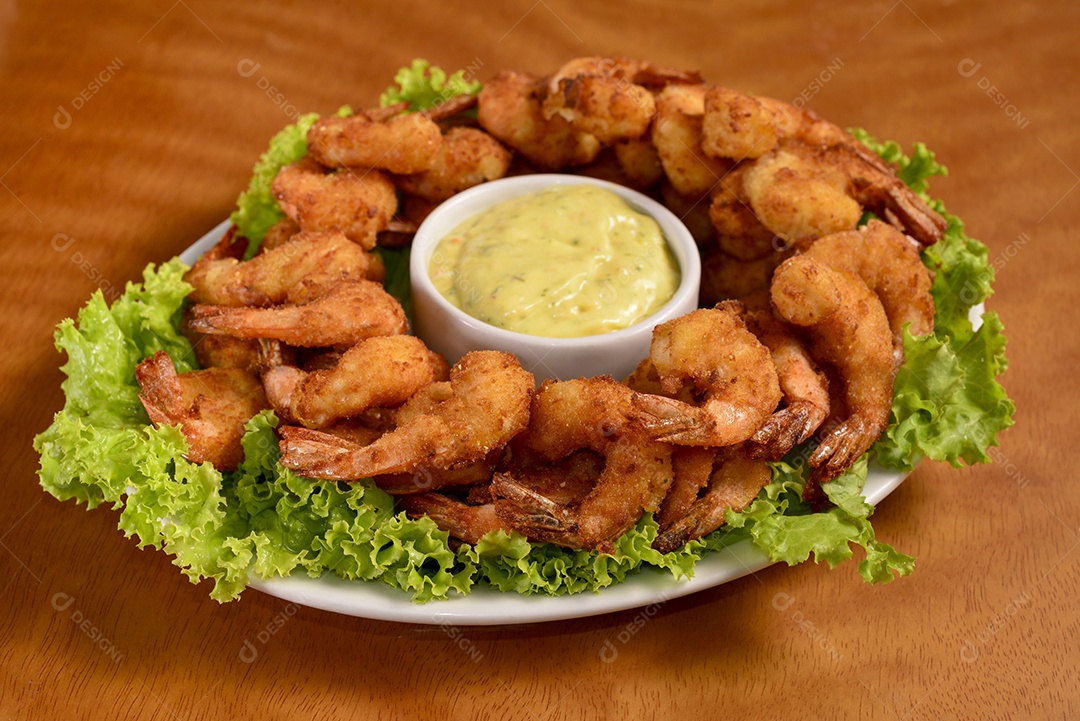 Camarão à milanesa com molho tártaro em chapa branca na mesa de madeira.