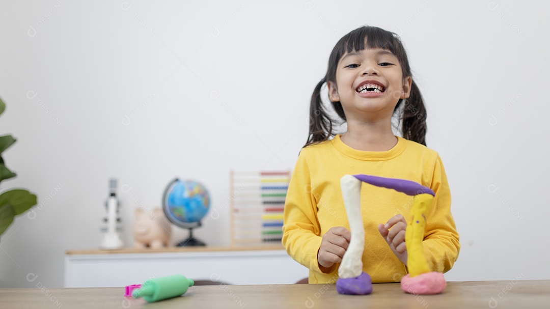 Garotinha está aprendendo a usar massinha colorida em uma sala