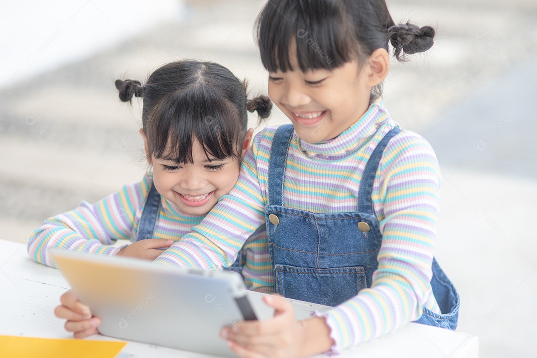 Duas irmãzinhas asiáticas brincando com um tablet digital em casa