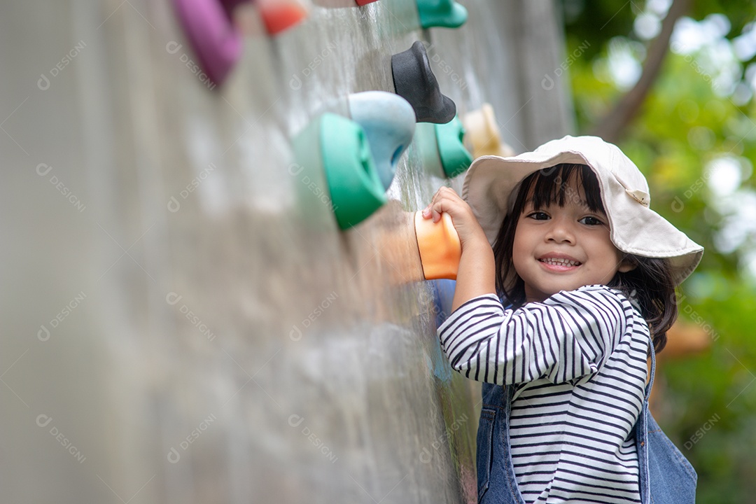Menina asiática escalando uma parede de pedra