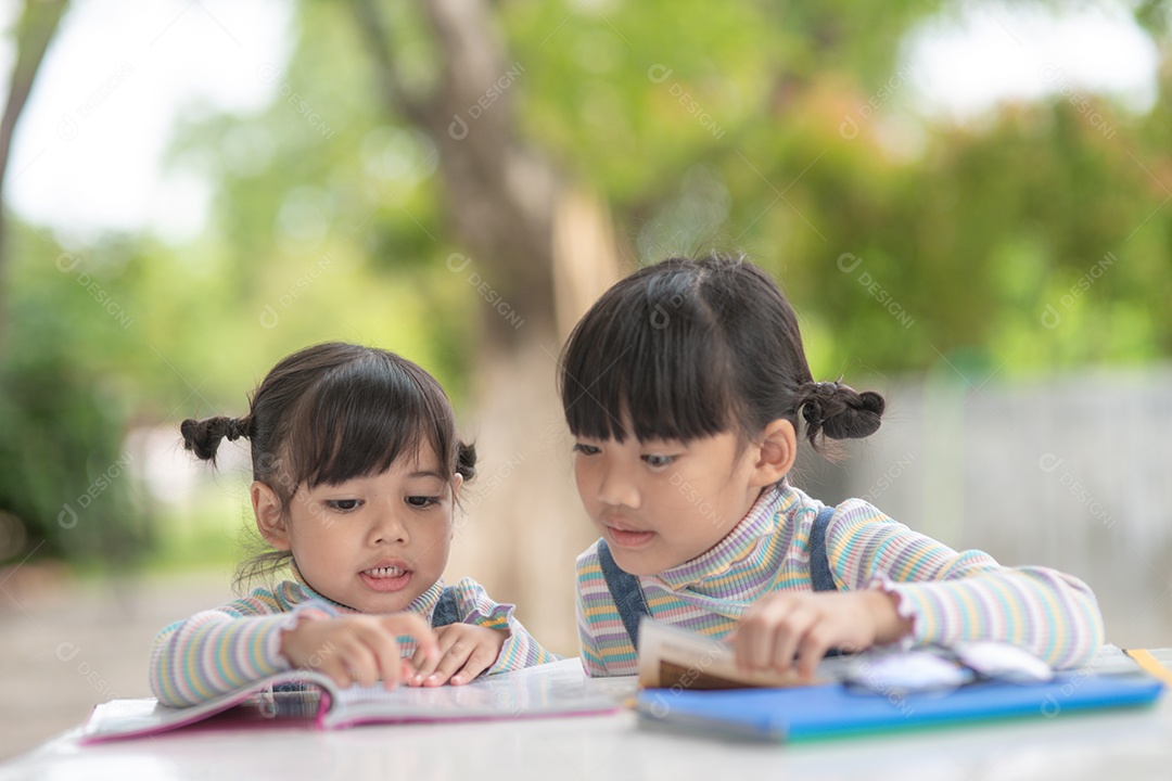 Duas meninas asiáticas estudantes lendo o livro na mesa.