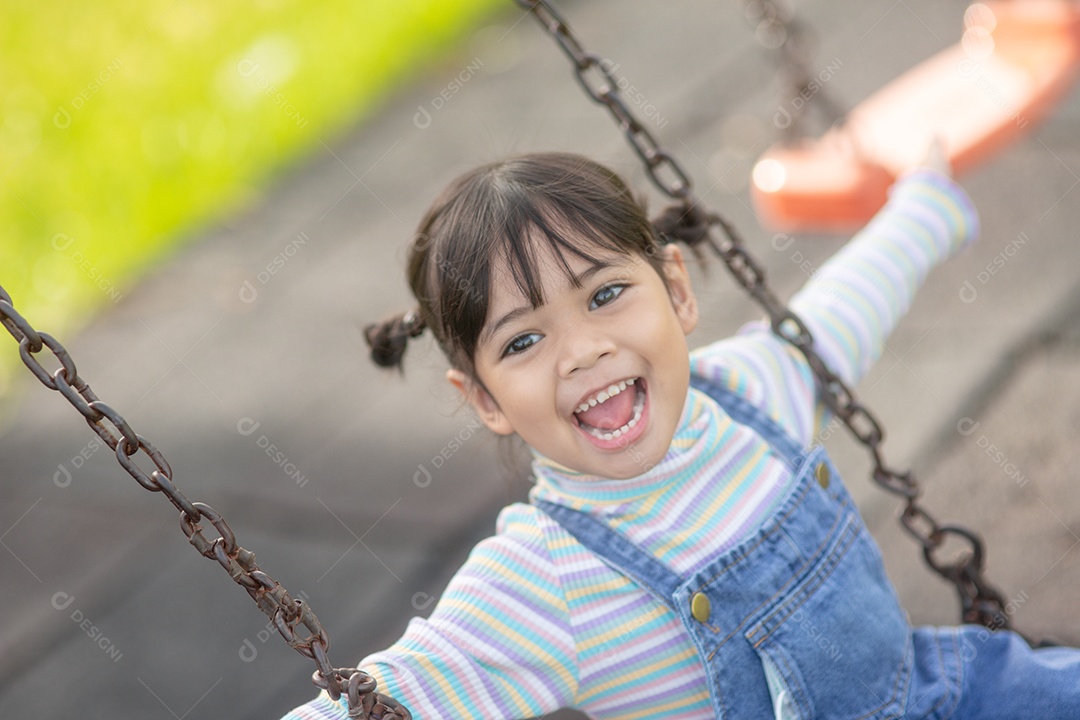 Menina asiática feliz jogando swing ao ar livre no parque.