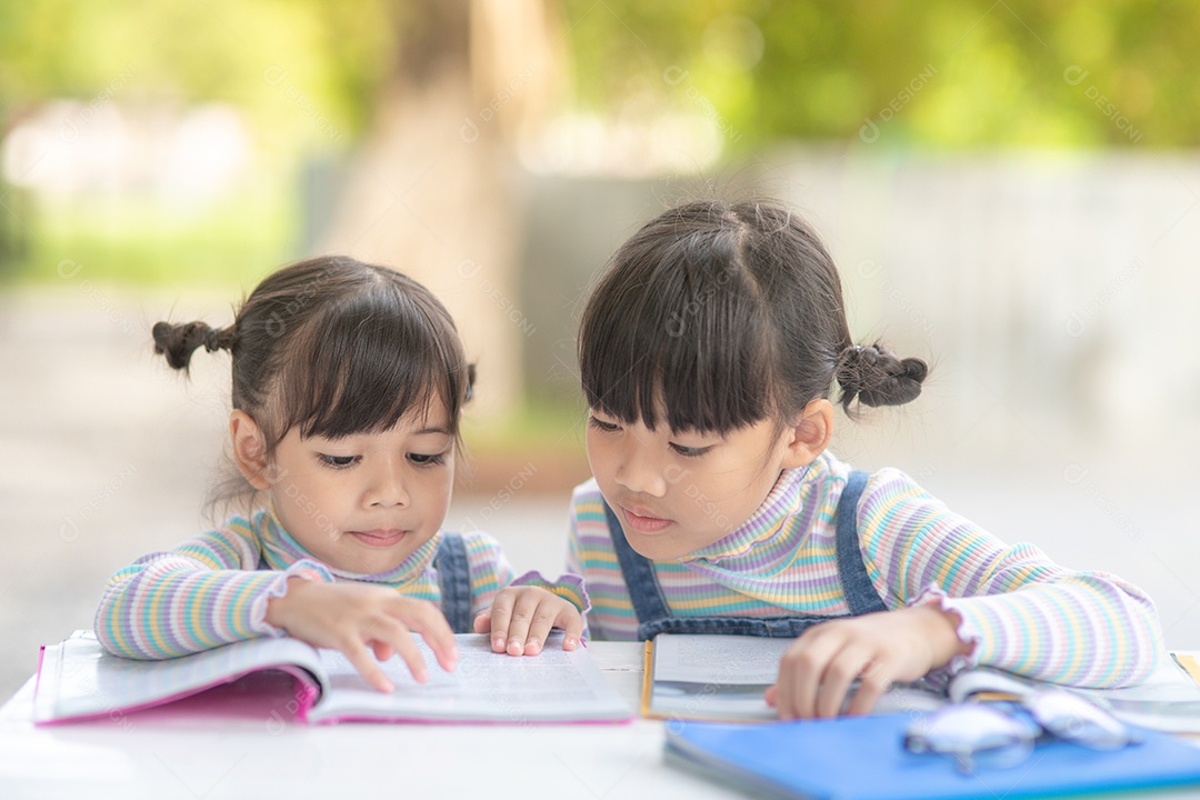 Duas meninas asiáticas estudantes lendo o livro na mesa.