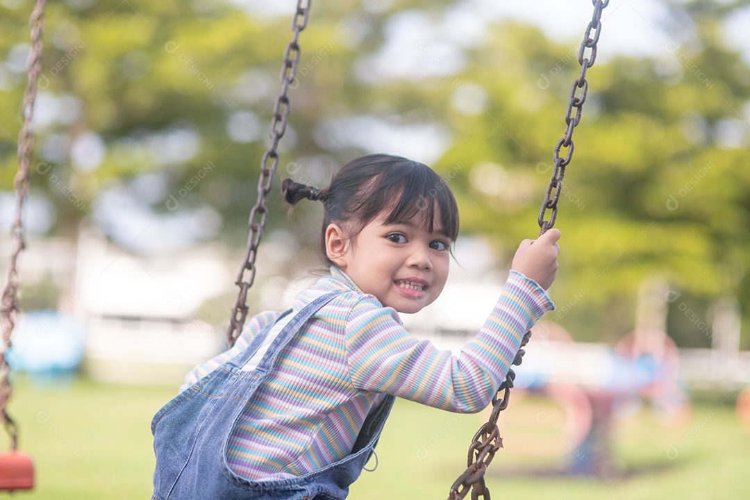 Menina asiática feliz jogando swing ao ar livre no parque.