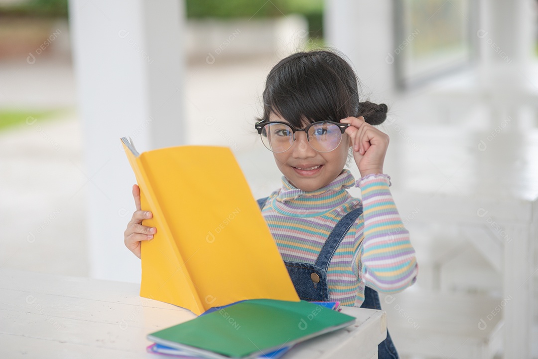 Menina asiática feliz lendo um livro sobre a mesa.