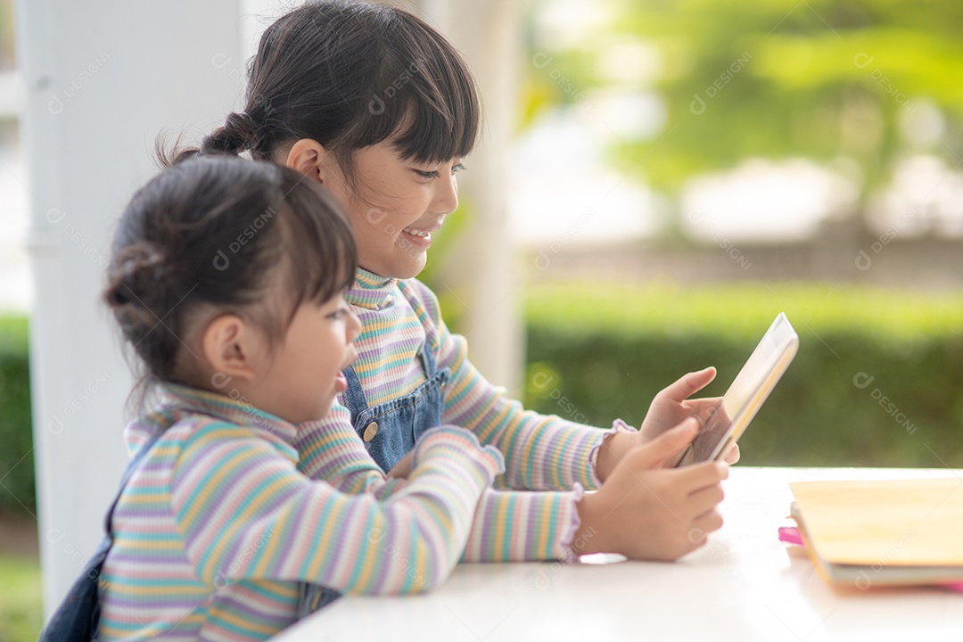 Duas irmãzinhas asiáticas brincando com um tablet digital em casa.