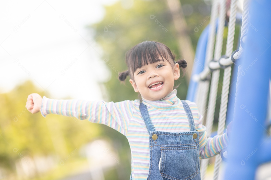 Crianças fofas. Garota asiática subindo em uma estrutura de playground de corda.
