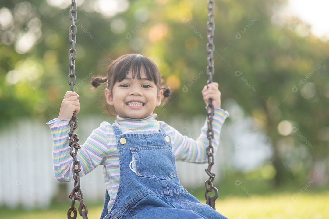 Menina asiática feliz jogando swing ao ar livre no parque.