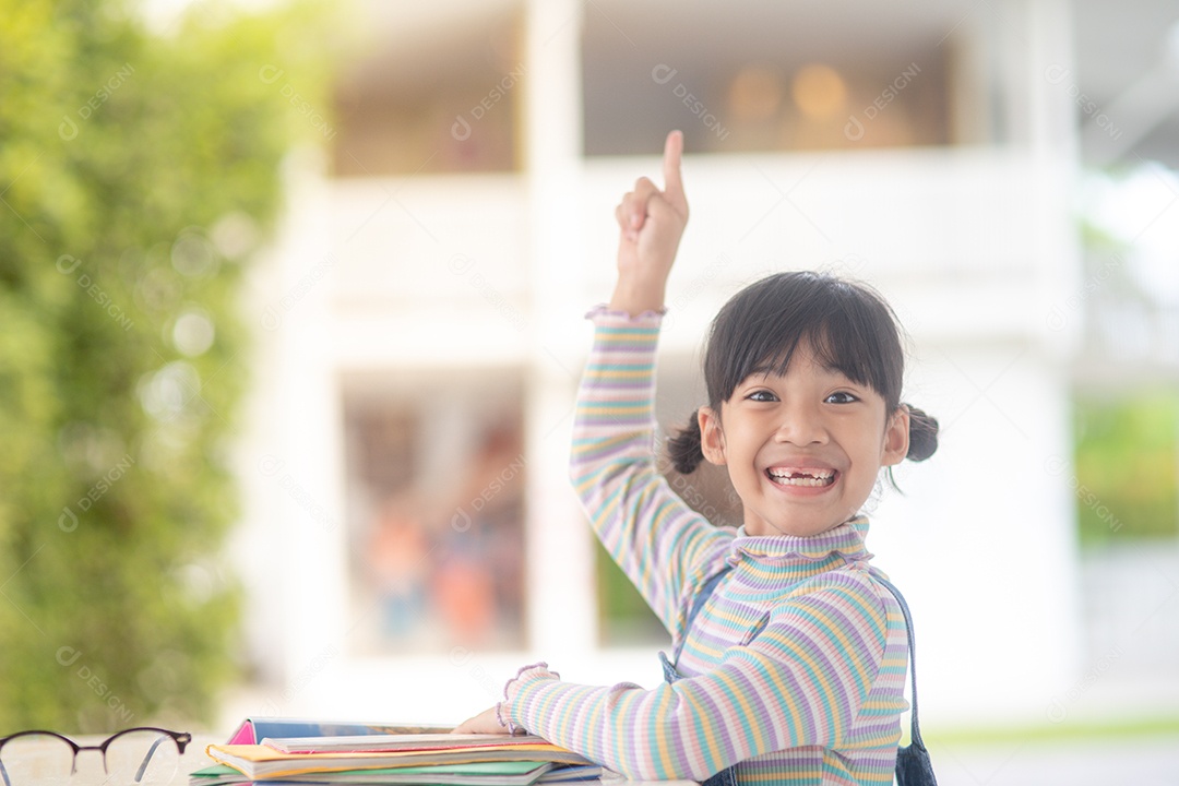 Menina asiática feliz lendo livro de histórias em cima da mesa.