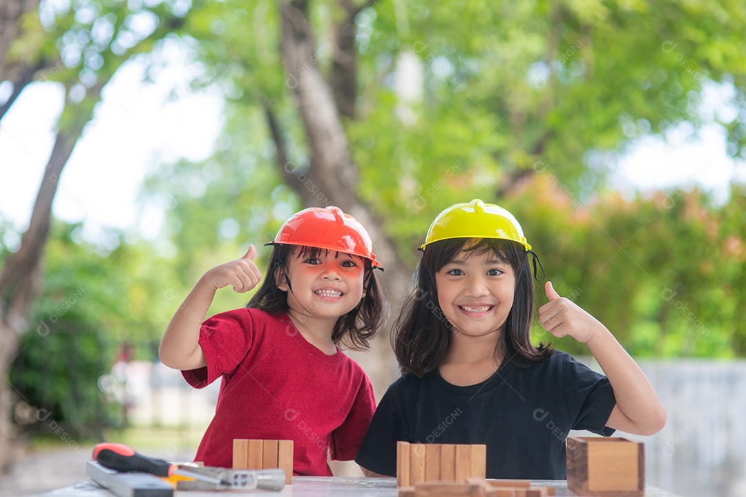 Meninas de irmãs asiáticas usando chapéus de engenharia construindo casa