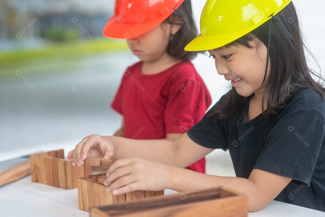 Meninas de irmãs asiáticos usando chapéus de engenharia construindo casa para