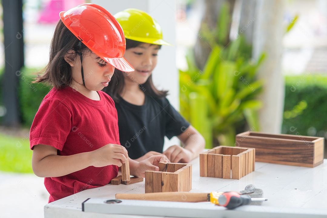 Meninas de irmãs asiáticos usando chapéus de engenharia construindo casa para