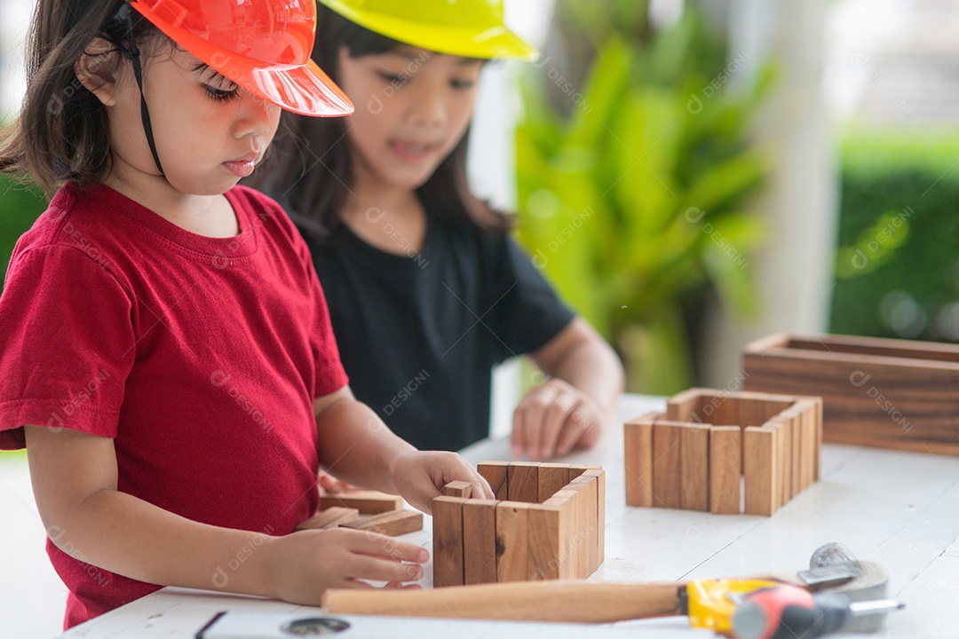 Meninas de irmãs asiáticos usando chapéus de engenharia construindo casa para