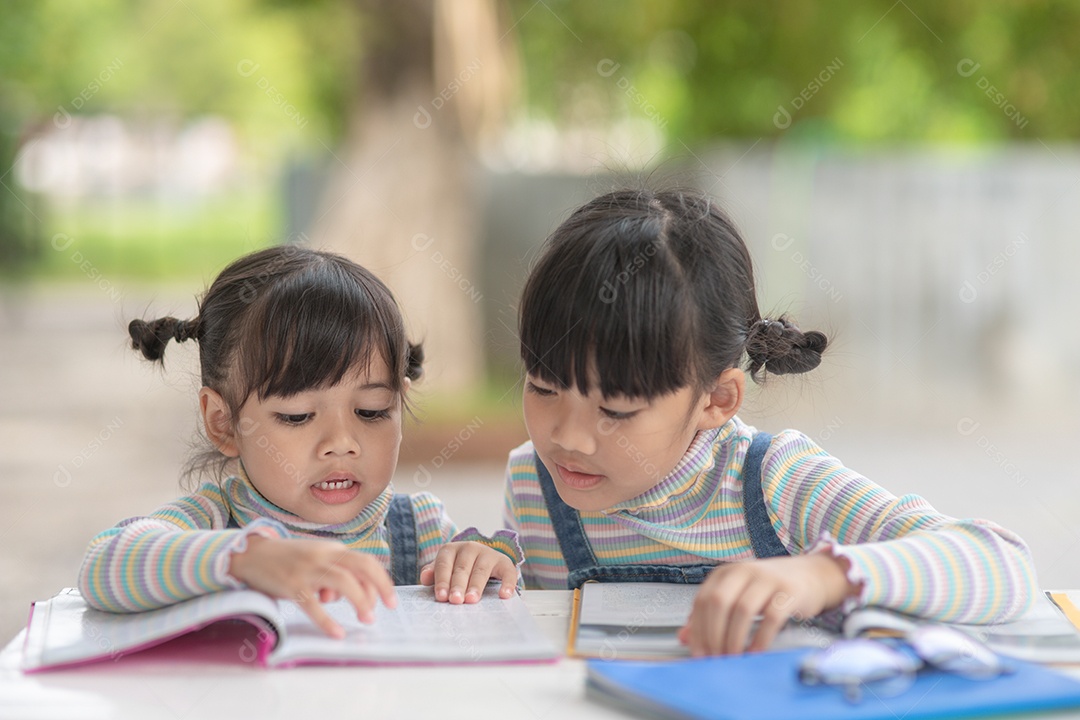 Girls and sisters reading a book together. Lovely Asian