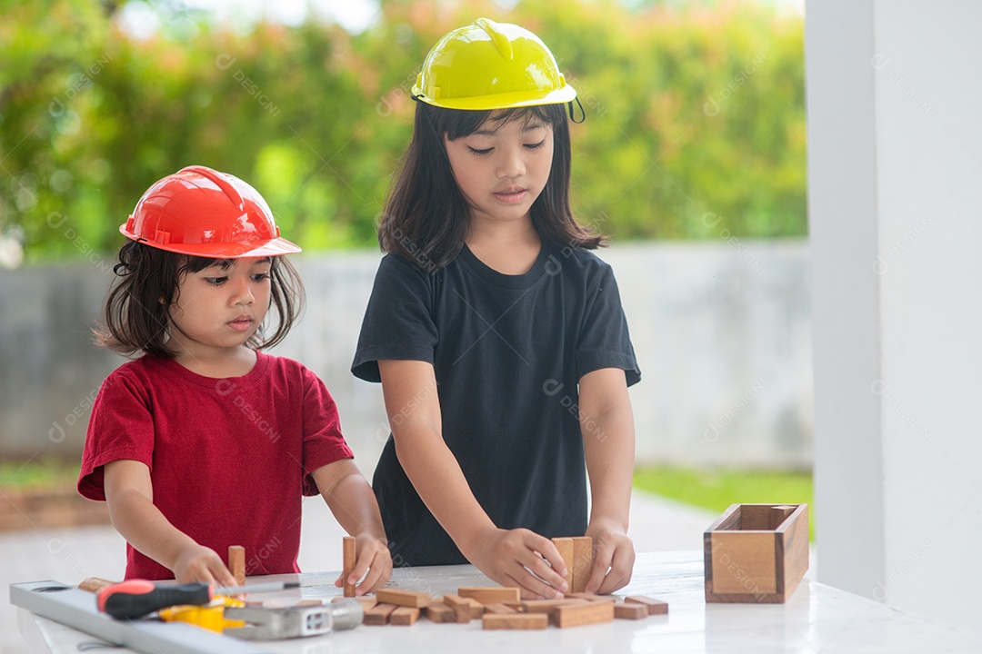 Meninas de irmãs asiáticas usando chapéus de engenharia construindo casa