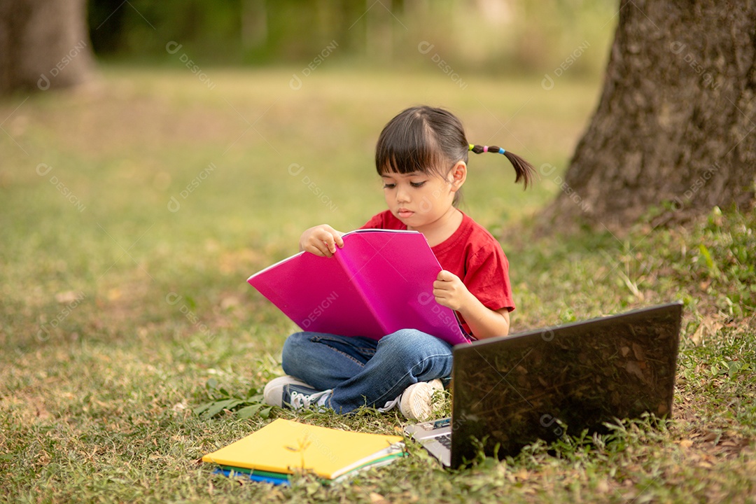 Menina bonitinha lendo livro sentado sobre gramado verde parque