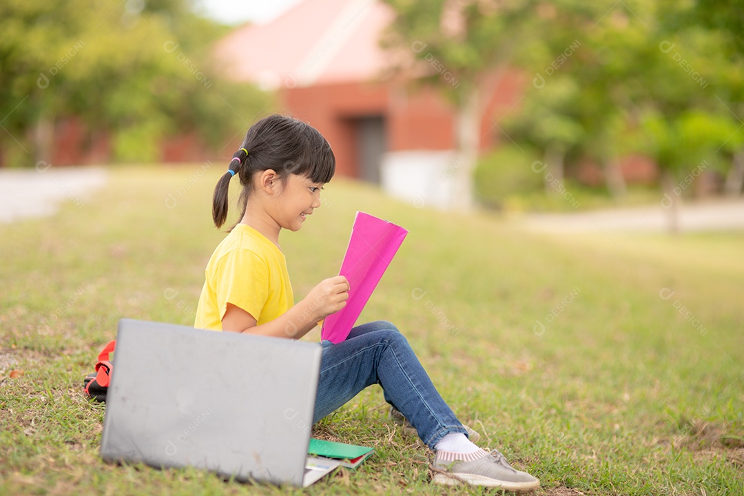 Cute little girl reading book sitting on green lawn in park