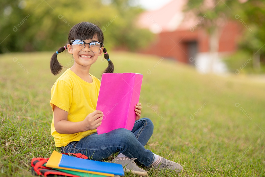 Menina bonitinha lendo livro sentado sobre gramado verde parque